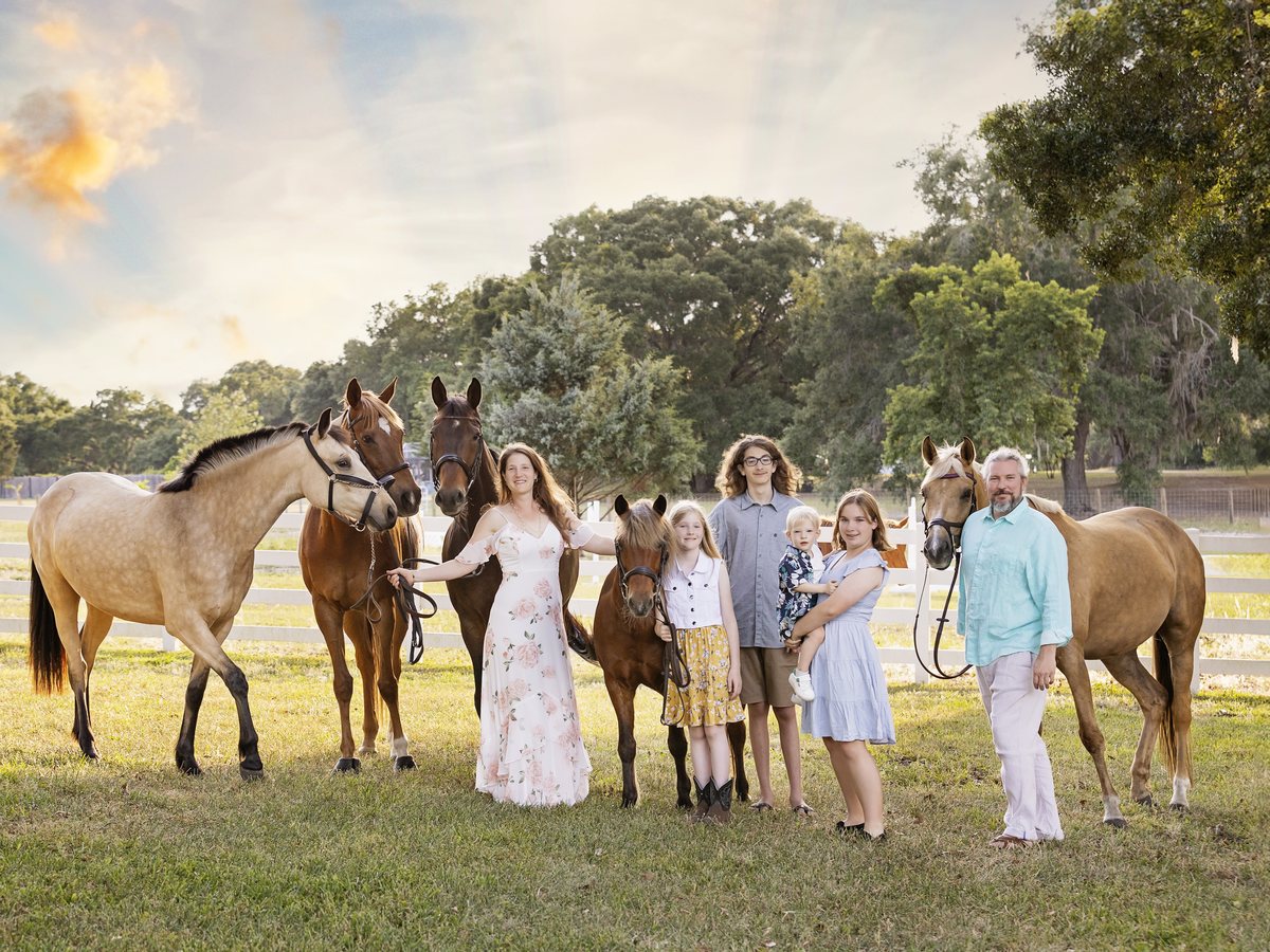 The family standing together in a field at sunset with four horses