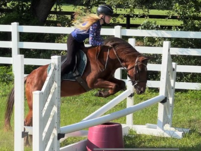 A young rider in a helmet jumping a palomino pony over a vertical